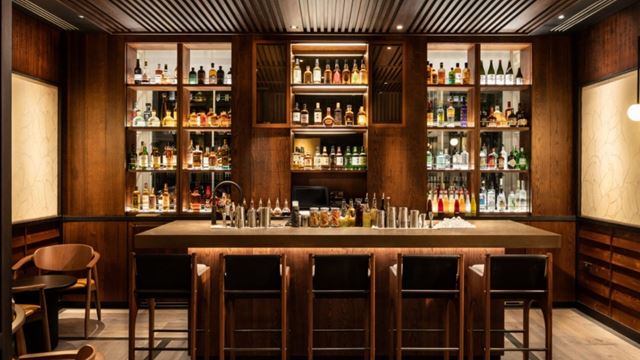 Bar with warm wooden interiors, black bar stools and shelves lined with Japanese whisky.